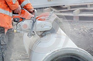 A worker at the construction site cutting concrete drainage pipe with a concrete saw..Builder covered in a hazardous dust cloud