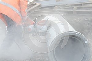 Worker at the construction site cutting a concrete drainage pipe with a concrete saw..Builder covered in a hazardous dust cloud