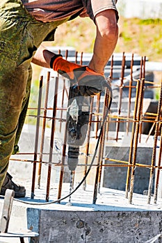 A worker at a construction site drills a reinforced concrete foundation with a puncher or drill to install the formwork.