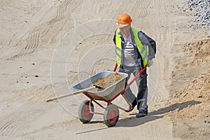 Worker at the construction site loads the shovel with sand in the wheelbarrow