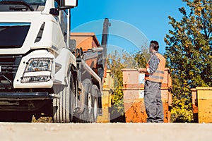Worker on construction site unloading container for waste from truck