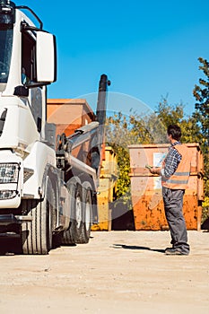 Worker on construction site unloading container for waste from truck