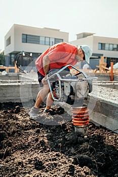 Worker on construction site with vibratory compactor for soil compacting or earth rammer