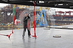 Worker in coveralls and hardhat with hose at industrial site.