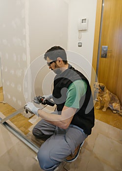 worker cuts aluminum profiles of plasterboard wall with grinder while dog watches carefully