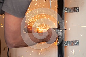 Worker cuts black metal installation with anelectric angle grinder, sparks fly around