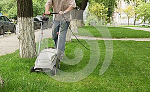 The worker cuts the high grass with an industrial electric lawn mower