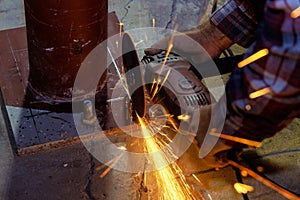 Worker cuts metal with an abrasive disk in an industrial factory with a spark while grinding iron