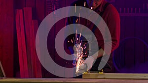 Worker cuts metal with angle grinder. Sparks and smoke fly in slow motion