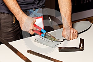 A worker cuts a sheet of roofing iron with metal scissors