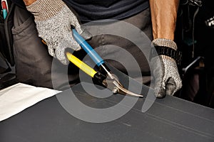 A worker cuts a sheet of roofing iron with metal scissors