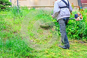 A worker cuts tall grass with an industrial petrol trimmer in hard-to-reach areas of a city lawn