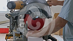 Worker cuts wood baseboard on the power miter saw