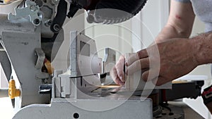 Worker cuts wood baseboard on the power miter saw