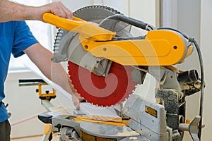 Worker cuts wood baseboard on the power miter saw new home