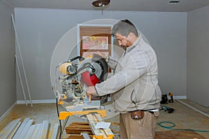 Worker cuts wood baseboard on the power saw