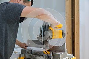 Worker cuts wood baseboard on the power saw