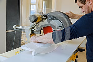 Worker cuts wood baseboard on the power saw