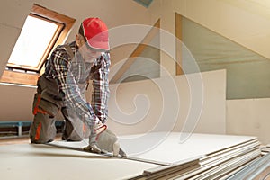 Worker cutting drywall plasterboard with construction knife. Attic renovation photo