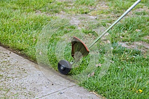 Worker in cutting grass the near pavement with using string lawn trimmer