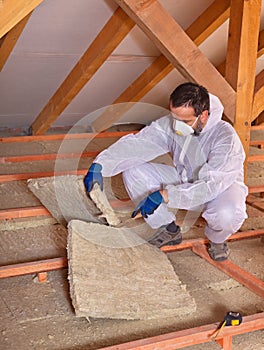 Worker cutting mineral wool panel to install thermal insulation