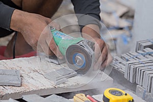 Worker cutting a sand stone tile using an angle grinder
