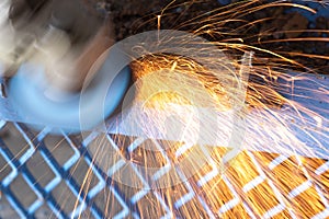 Worker cutting steel with grinding machine and splashes of sparks in workshop