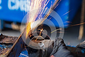 Worker cutting steel with grinding machine and splashes of sparks in workshop