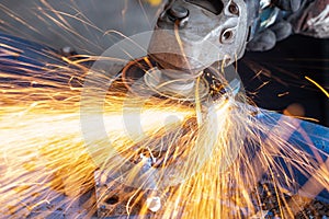 Worker cutting steel with grinding machine and splashes of sparks in workshop