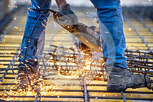 Worker cutting steel, sawing reinforced bars using angle grinder mitre saw