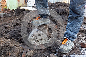 Worker in dirty uniform and shoes with orange laces is staying in the stone in construction site. Concept of diry and