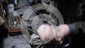 Worker is disassembling car engine in a repair shop, twisting bolts and detaching details with force