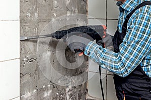 A worker dismantles facing tiles in the bathroom using a perforator