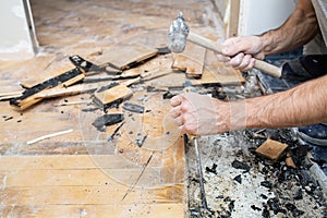 A worker dismantles the old parquet floor with a hammer and chisel. Renovation in the apartment