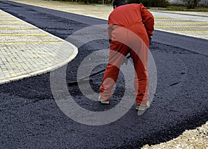 Worker distributes on the edge the asphalt laid