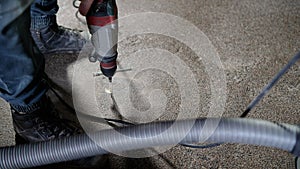 A worker drills into a concrete floor using a drill, close-up. Drilling a floor in concrete. A builder drills into a