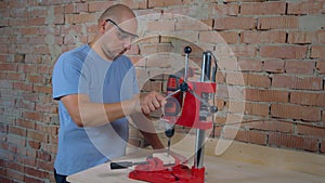 Worker drills hole in wooden board with machine tool in workshop.