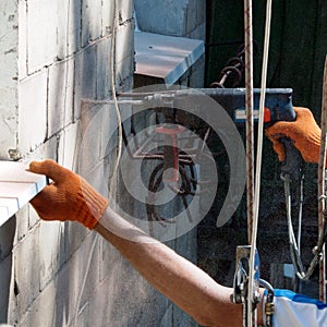 A worker drills the wall of multistory building with an electric drill.