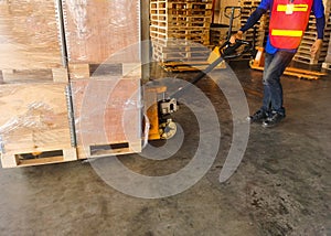 Worker driving forklift loading shipment carton boxes and goods on wooden pallet at loading dock from container truck to warehouse