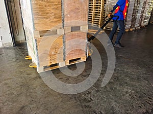 Worker driving forklift loading shipment carton boxes and goods on wooden pallet at loading dock from container truck to warehouse