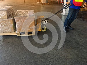 Worker driving forklift loading shipment carton boxes and goods on wooden pallet at loading dock from container truck to warehouse