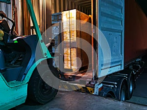 Worker driving forklift loading shipment carton boxes goods on wooden pallet at loading dock from container truck to warehouse car photo