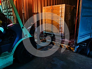 Worker driving forklift loading shipment carton boxes goods on wooden pallet at loading dock from container truck to warehouse