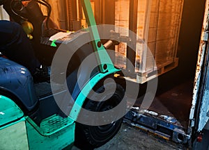 Worker driving forklift loading shipment carton boxes goods on wooden pallet at loading dock from container truck to warehouse car