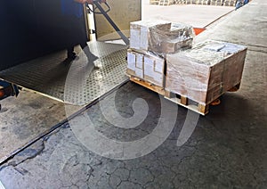 Worker driving forklift loading shipment carton boxes goods on wooden pallet at loading dock from container truck to warehouse car