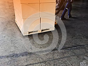 Worker driving forklift loading shipment carton boxes goods on wooden pallet at loading dock from container truck to warehouse car