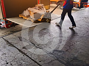 Worker driving forklift loading and unloading shipment carton boxes and goods on wooden pallet from container truck to warehouse c