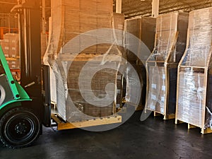 Worker driving forklift loading and unloading shipment carton boxes and goods on wooden pallet from container truck to warehouse c