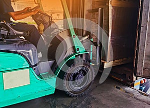 Worker driving forklift loading and unloading shipment carton boxes and goods on wooden pallet from container truck to warehouse c