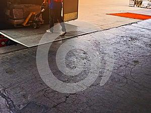 Worker driving forklift loading and unloading shipment carton boxes and goods on wooden pallet from container truck to warehouse c